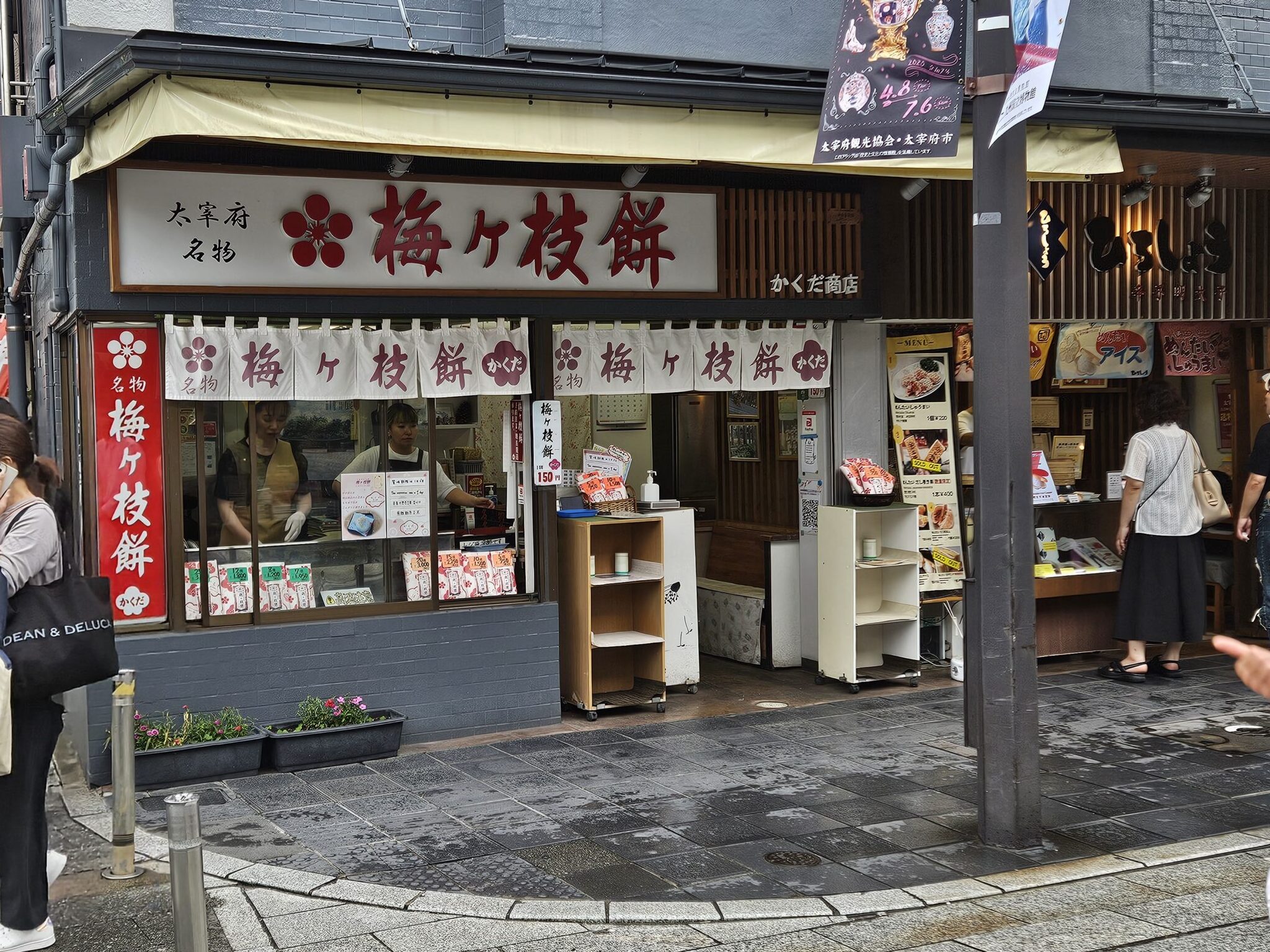 Exterior of Kakuda Shoten, a traditional Umegae Mochi shop along the approach to Dazaifu Tenmangu Shrine. Visitors can watch the mochi being hand-grilled at the storefront, surrounded by the cozy aroma of freshly toasted rice cakes.