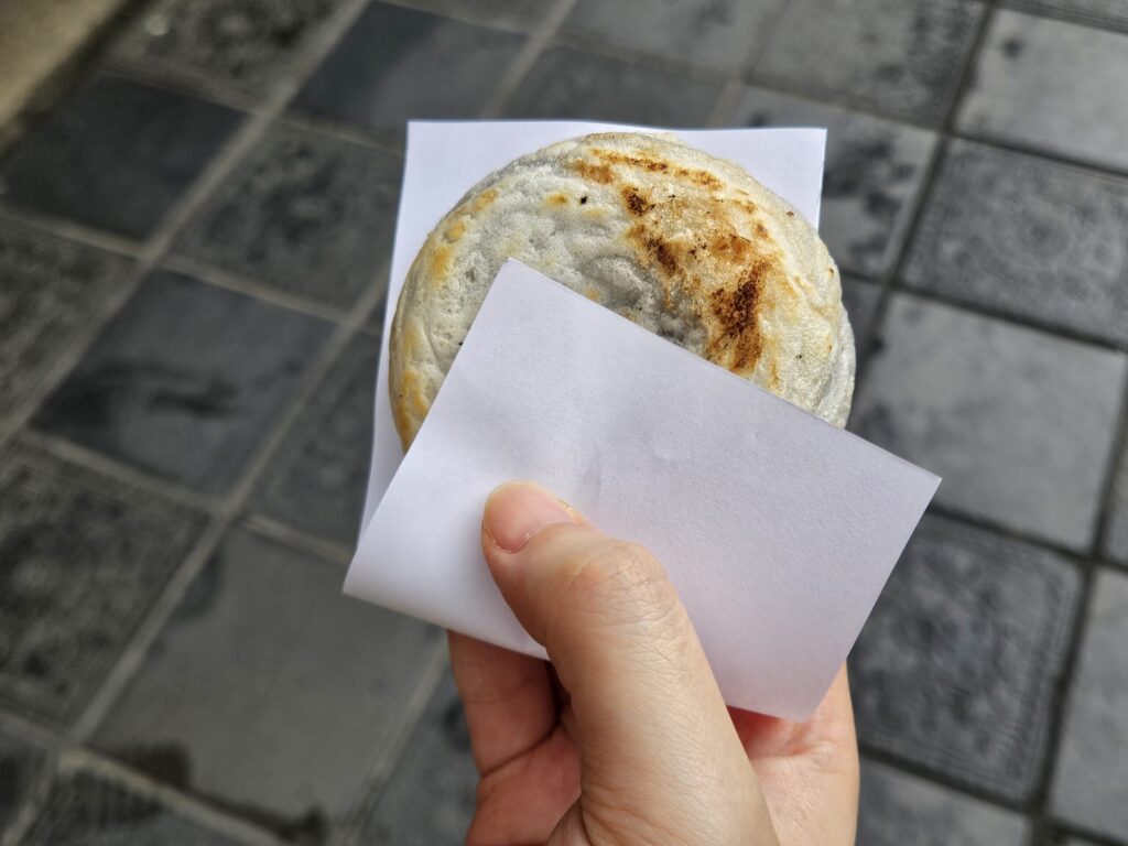 Holding a freshly baked Umegae Mochi from Tenmanya in front of Dazaifu Tenmangu Shrine, captured in the right hand.
