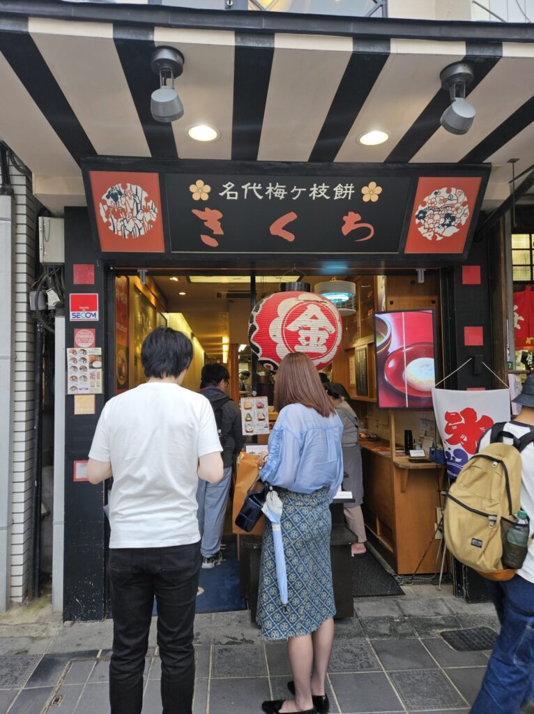 Exterior of Kikuchi, a popular Umegae Mochi shop on the approach to Dazaifu Tenmangu Shrine. The shop is often crowded on weekends, with lines of visitors waiting as freshly grilled mochi fill the air with a toasty aroma.