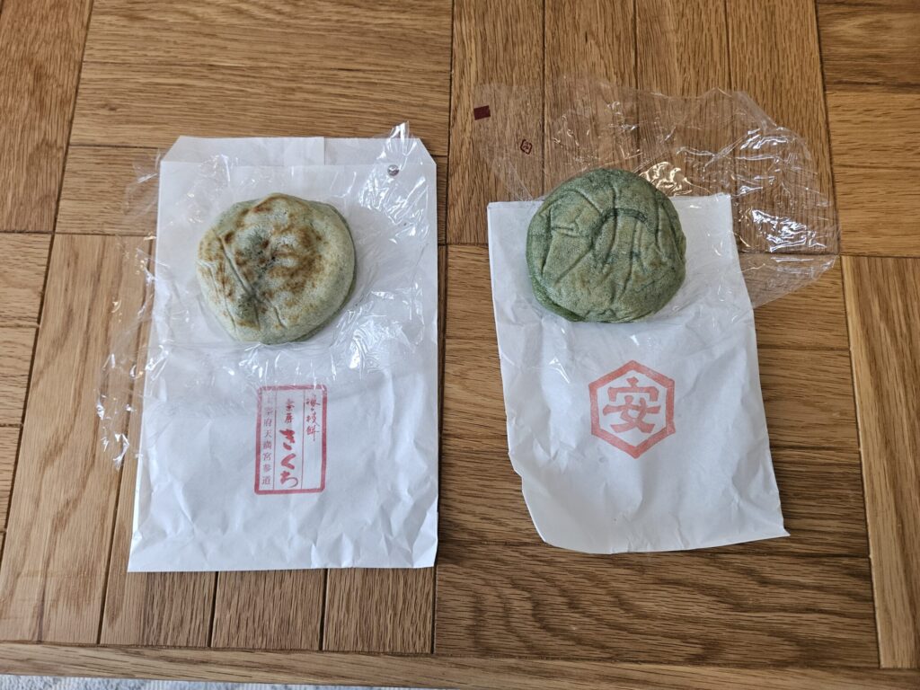 Yomogi (mugwort) Umegae-mochi from two famous Dazaifu shops, Kikuchi and Yasutake, displayed side by side on a table.