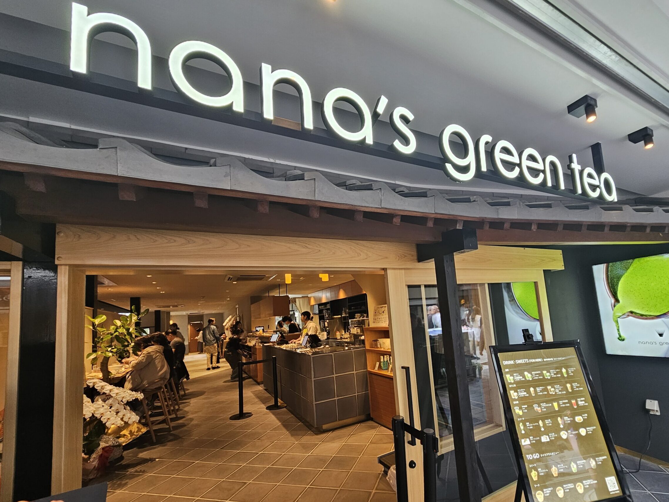 Entrance of nana’s green tea Dazaifu Sando Café, featuring matcha-themed displays and a warm, inviting atmosphere.