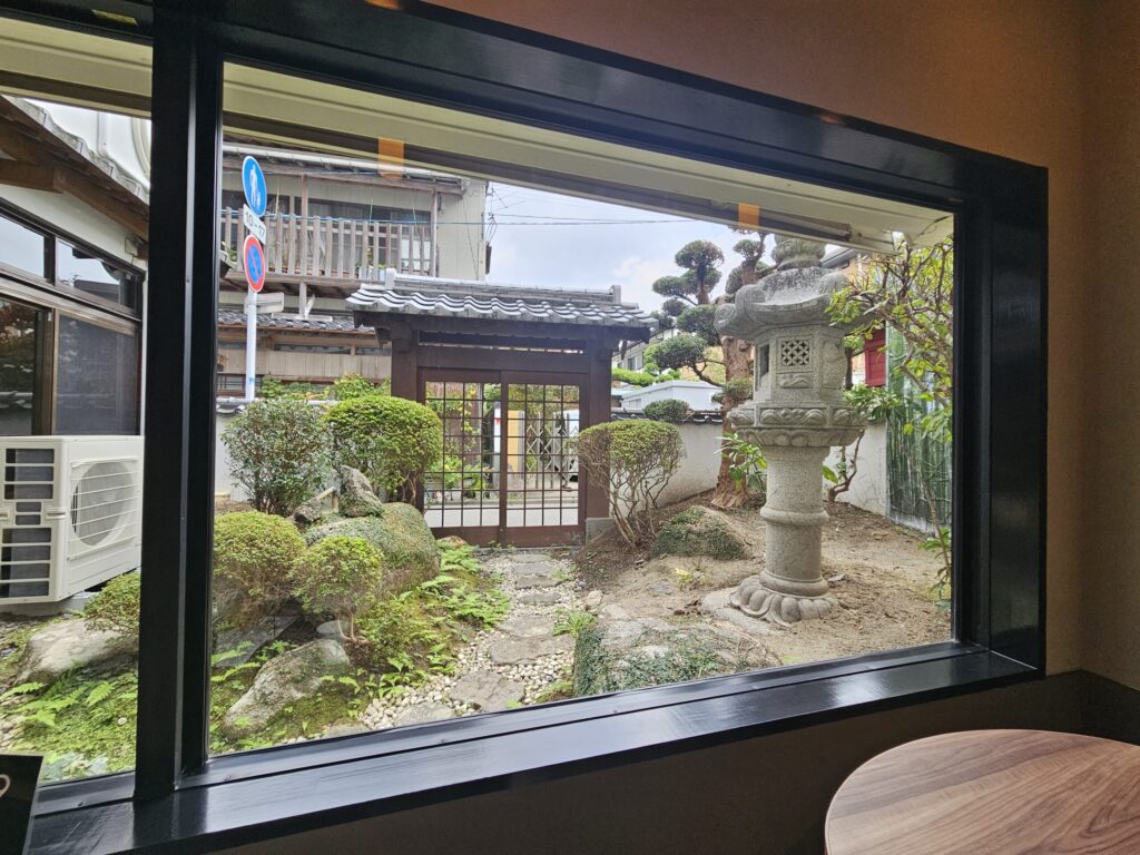 View of a peaceful Japanese-style garden from the window seats at nana’s green tea Dazaifu Sando Café.