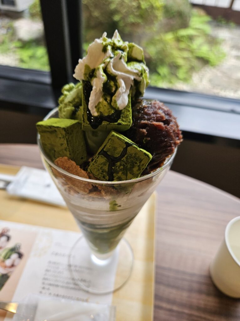Close-up of a matcha nama chocolate parfait topped with soft serve ice cream, red bean paste, and rich matcha chocolate.