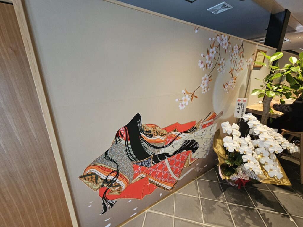 Traditional Japanese-style painting of a Heian-era woman in a junihitoe kimono at the entrance of nana’s green tea Dazaifu Sando Café.